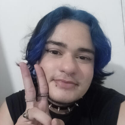 Selfie minha (Alex). Sou uma pessoa não-binária branca, tenho cabelo médio, azul na frente e preto atrás e tenho 3 piercings no rosto. Estou usando uma camisa preta, um choker preto com spikes e estou fazendo o símbolo da paz.